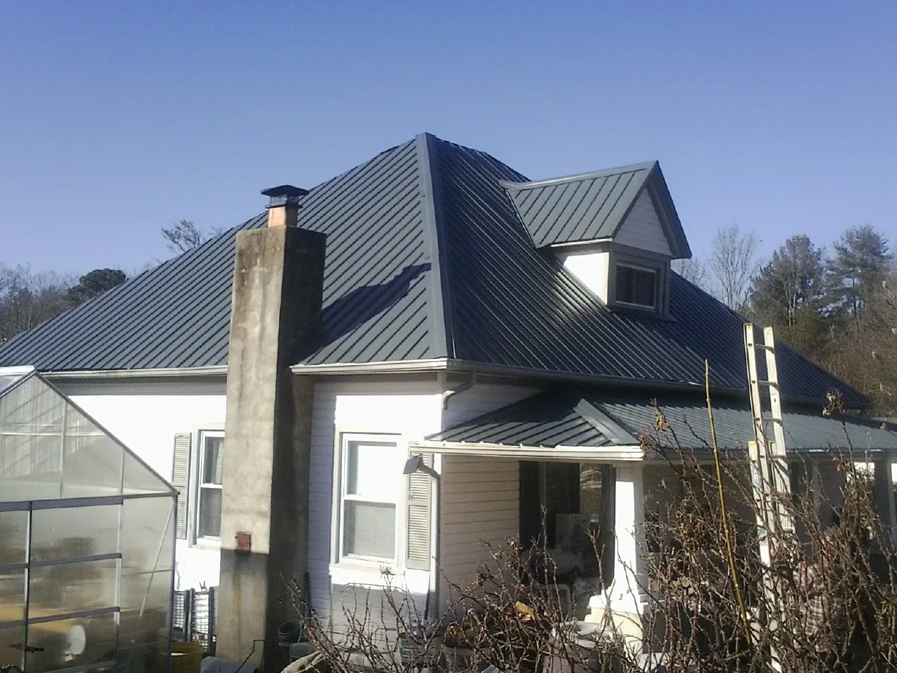 Dark blue standing seam metal roof on a white farmhouse with dormer — Slate & Tile Roof Repair by Roofing Brothers in Lithonia