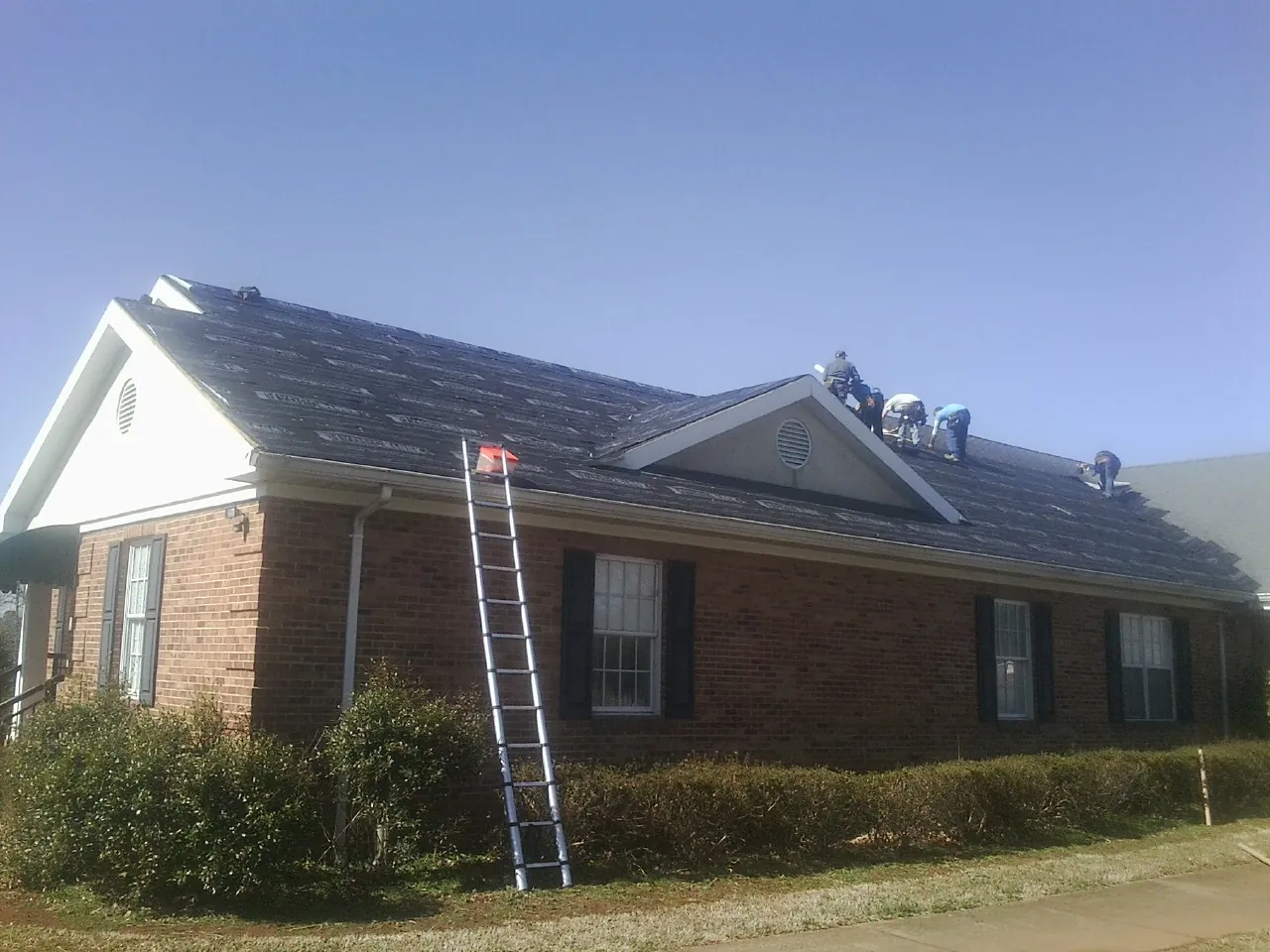 Crew tearing shingles off a brick ranch roof with a ladder set — Metal Roof Repair work by our crew in Lithonia
