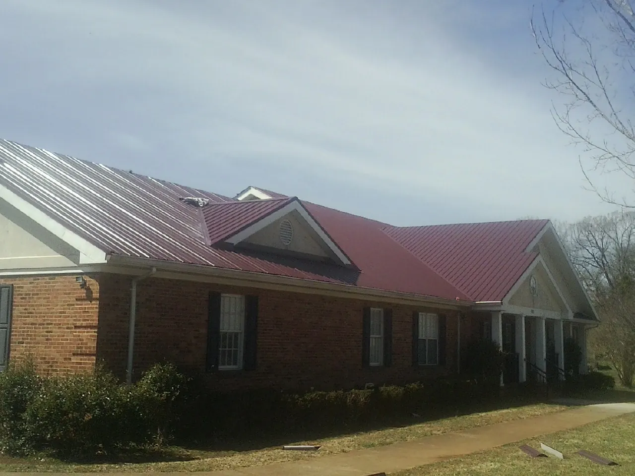 Red metal roof with gabled entries on a long brick building, from a Hail Damage Roof Repair job in Lithonia