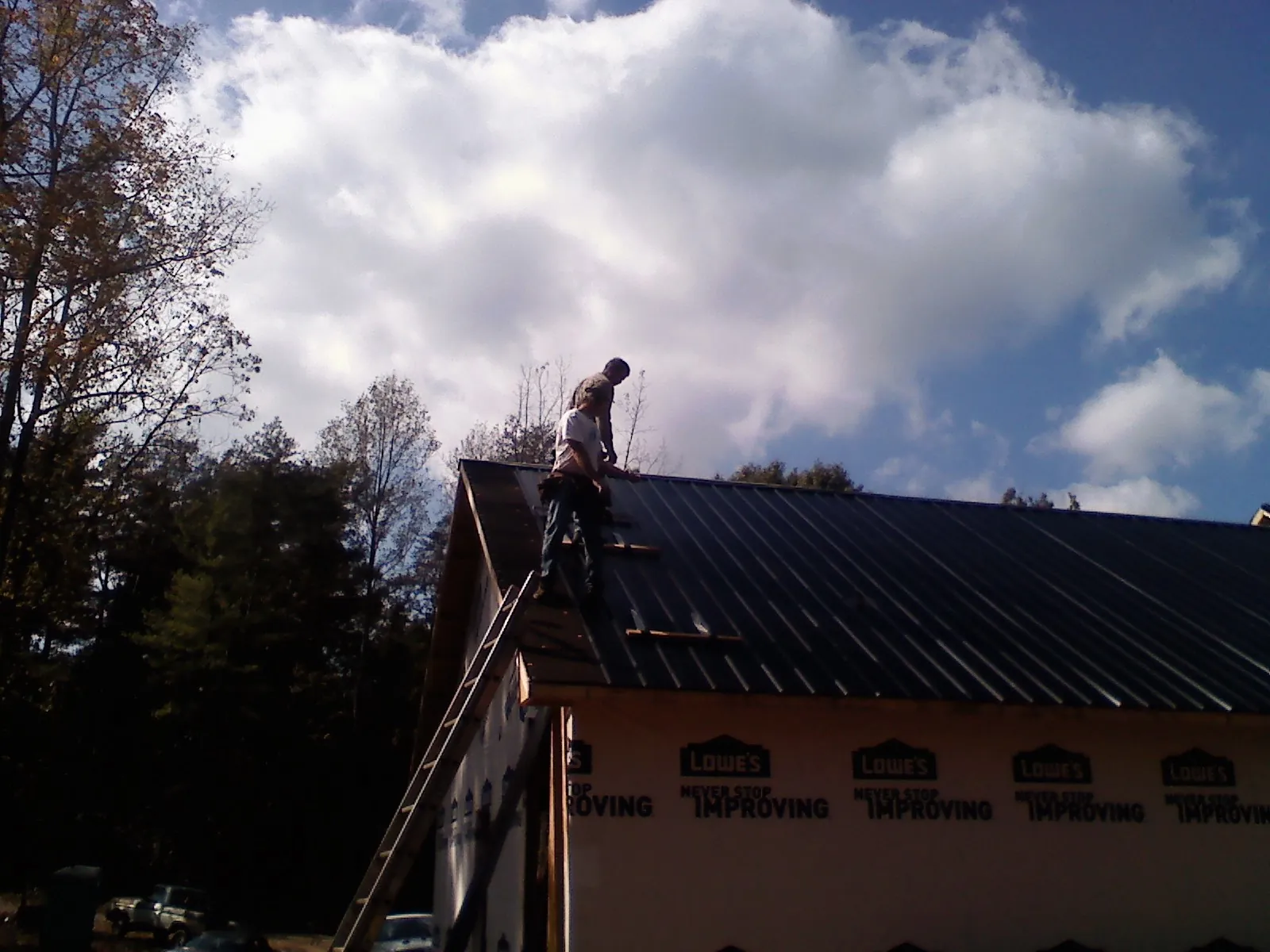 Roofer fastening dark metal panels high against a cloudy sky, from a Roof Inspection job in Lithonia