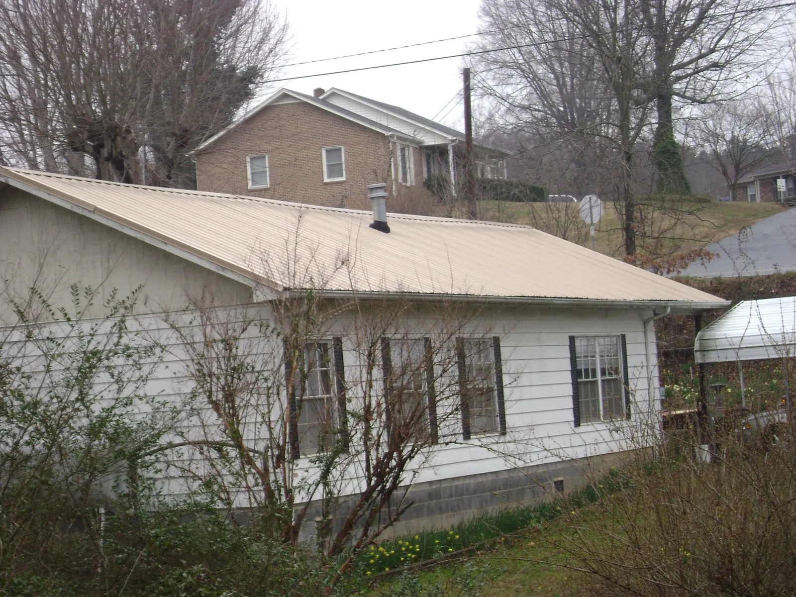Tan metal roof on a white sided house set into a hillside — Commercial Roofing by Roofing Brothers in Lithonia